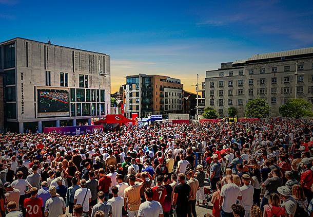 A large crowd of fans gathered in a sunny Millennium square to watch a live sporting event on the big screen.