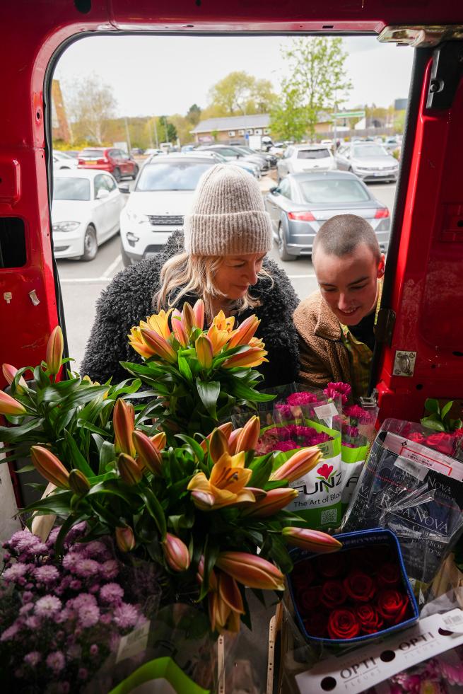 Two people look at a bunch of flowers in a van
