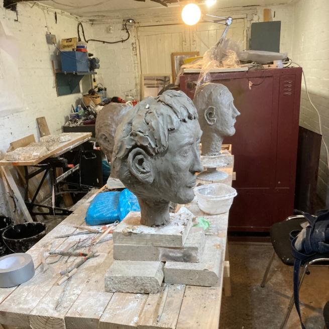 Three clay busts are on a wooden work bench