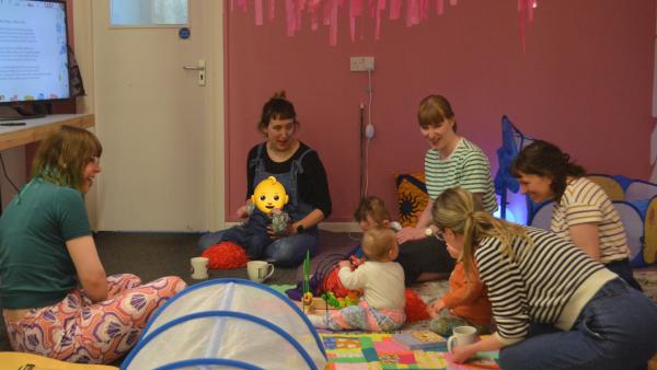 Five adults and four little ones enjoying toys and singing together.