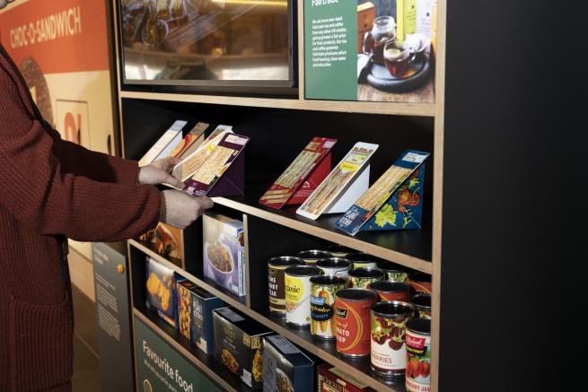A colour image of open shelves with replica food items and a person picking some of them up.