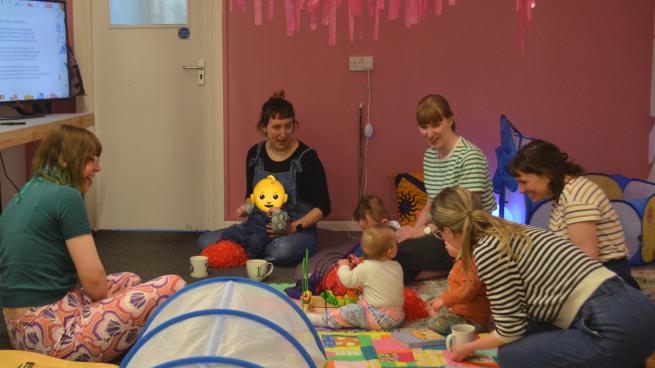 Five adults and four little ones enjoying toys and singing together.