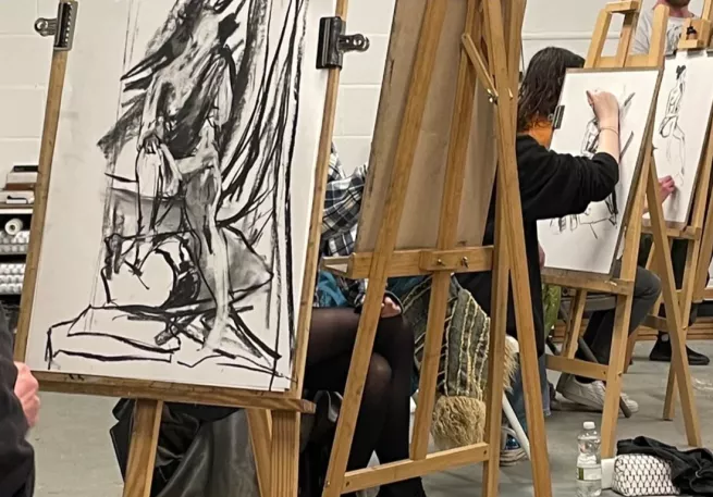 Artist sat at easels making charcoal drawings