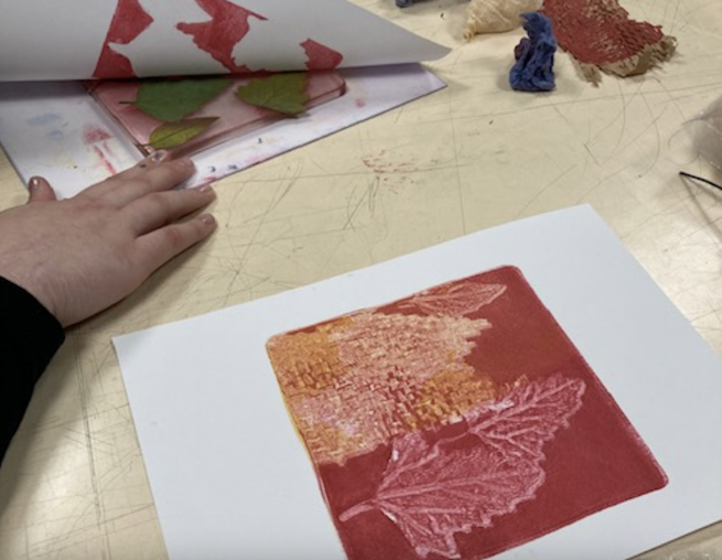 An image showing a red and orange gelli plate being printed using leaf patterns