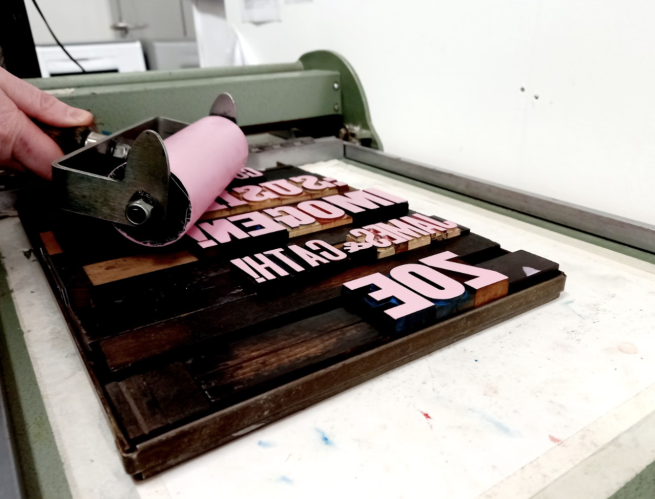Woodtype being prepared for printing from by being coated in pink ink with a roller 
