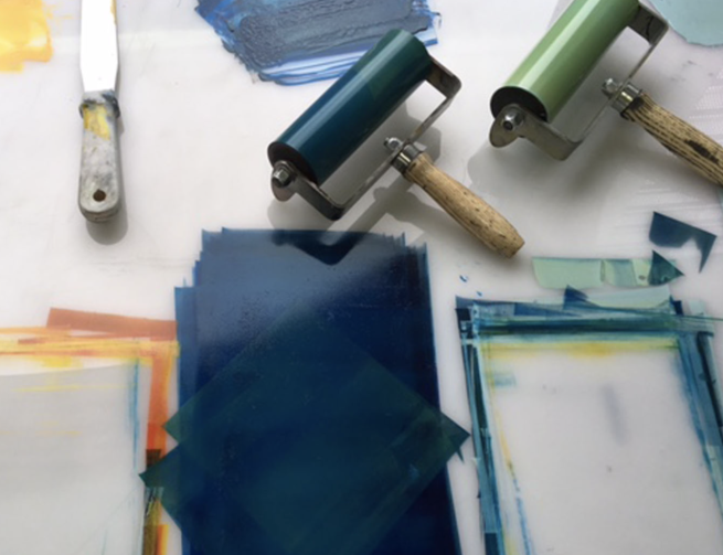 Printmaking rollers coated in blue and green ink with a pallete knife