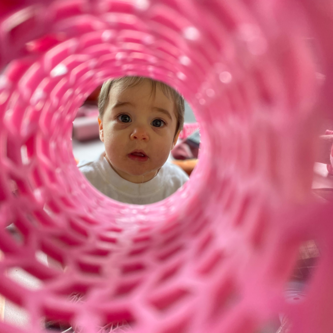 a baby looking through a pink tube
