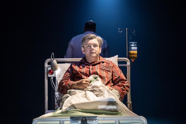 A still from Nye featuring Nye Bevan (played by Michael Sheen) sat up in a hospital bed.