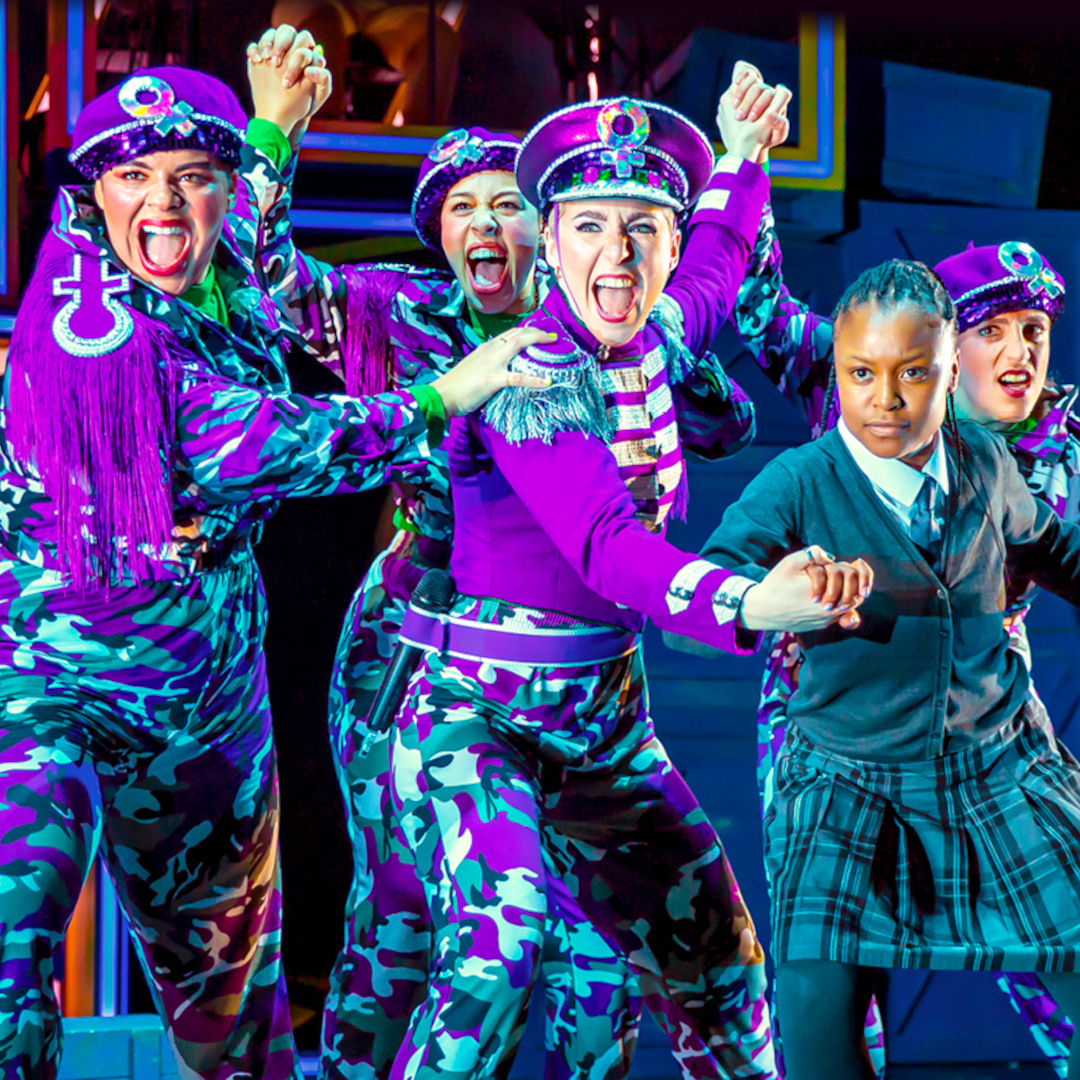 A group of women in purple and green camo dancing on stage with a young person. 