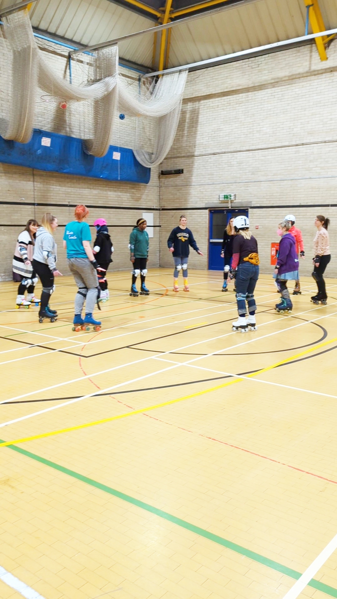 A coach on skates talks to a group of adult participants on roller skates 