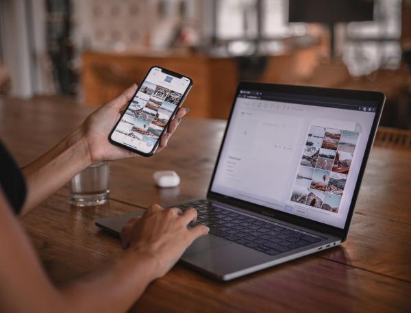 A person sat at a table using a laptop and holding a smartphone