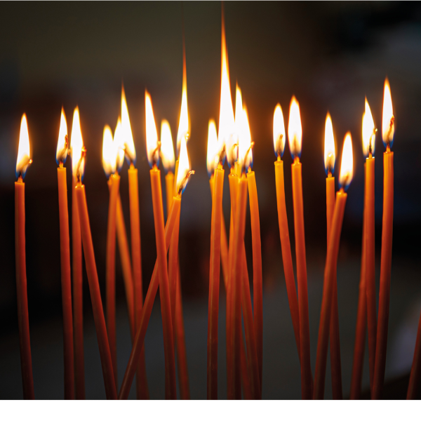 Candles stand together lit, in the dark.