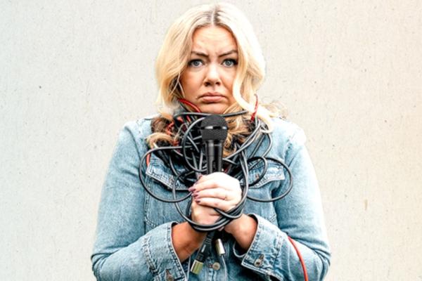 Serena Terry holding a black microphone with the cord tangled around her neck and upper torso.