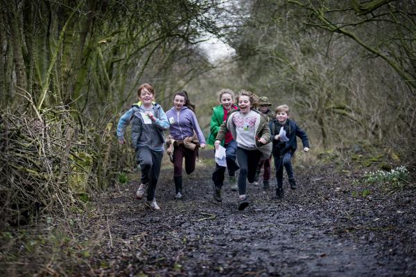 A photo of a group of children running along a path in the woods towards the camera.