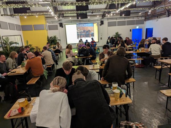 People sitting at tables playing boardgames. The people on the closest table are leaning very close to the table, concentrating hard.. 