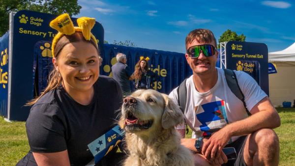 Two people crouching down smiling to camera with a retriever dog sitting centrally. 