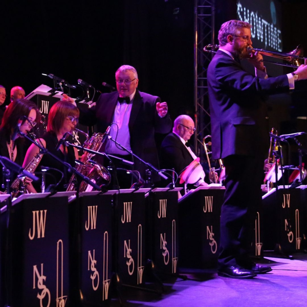 Members of the Northern Swing Orchestra on stage including the conductor and a trombonist standing up to do a solo.