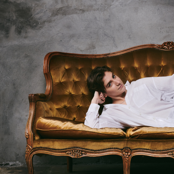 Sarah Keyworth wearing a white cotton shirt lying on a gold velvet sofa with a grey background.