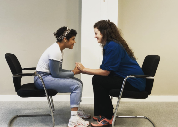 2 actors sitting across from one another in a Meisner exercise, holding hands and smiling at each other