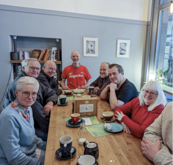 LGBT people across generations smiling sat around a table in a cafe