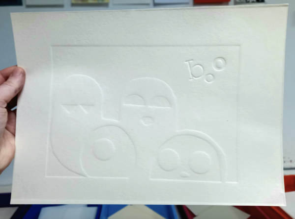 An image of a white piece of paper which has some ghosts and the word 'boo' embossed onto it