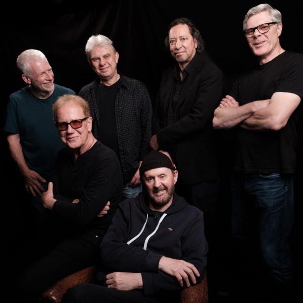 The six members of Oysterband wearing black on the top against a plain black background.