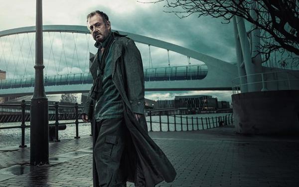 A haggard man in a jacket stood in front of a bridge.