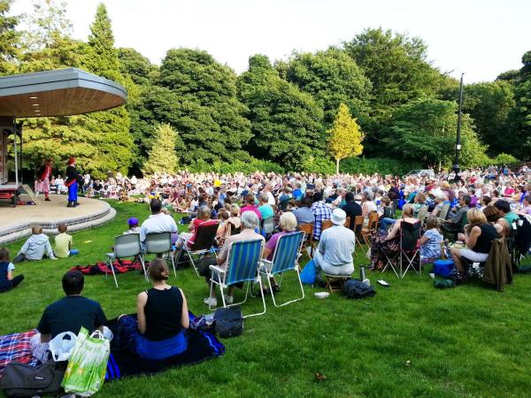 Audience sat watching a band in a park.