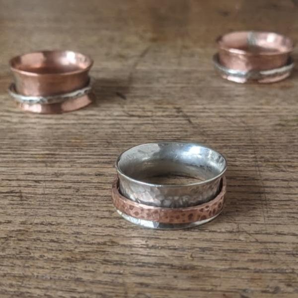 three silver and copper spinning rings lay on a wooden table