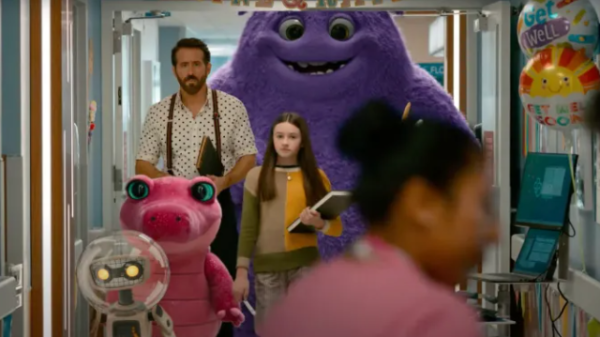 In a hospital, a nurse is in the foreground with balloons saying Get Well Soon. Blue a big furry purple imaginary friend is the furthest behind, in front of Blue is Calvin played by Ryan Reynolds, in a shirt and braces. Bea is in front of him with long brown hair and wearing a jumper that is purple and orange and jeans and is holding a book.In front of her is a pink short alligator imaginary friend. In front of the alligator is a robot like imaginary friend with a bubble sphere