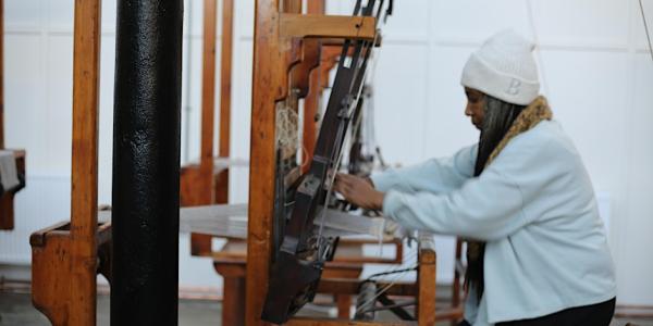 Image shows a woman working on an old traditional dobby loom.
