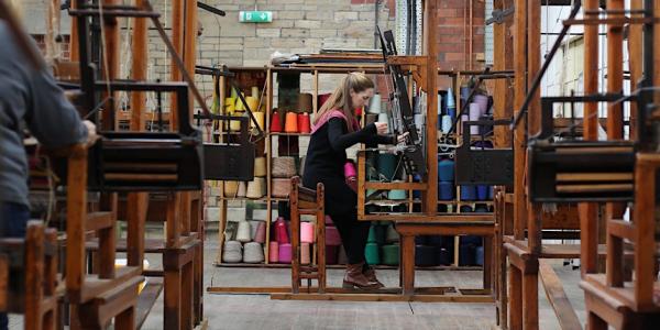 Image shows a workshop participant working on a traditional wooden dobby loom