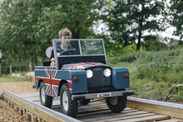 A small boy riding in a blue mini rover with the british flag on the side