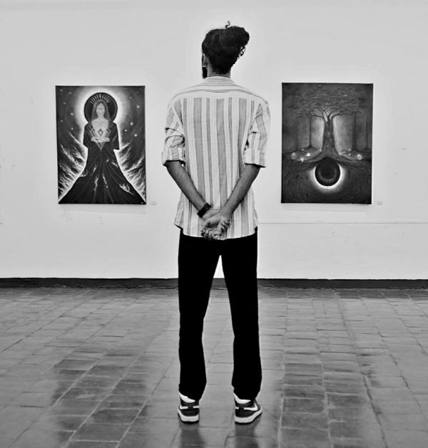 A black and white photograph featuring a person standing in front of two paintings on the wall.