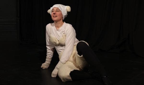 A woman with a DIY sheep outfit leans on the floor. Black background in a theatre