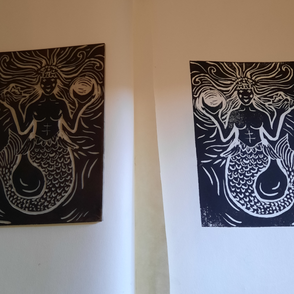 a print of a mermaid in black in and the lino from which the print was taken.