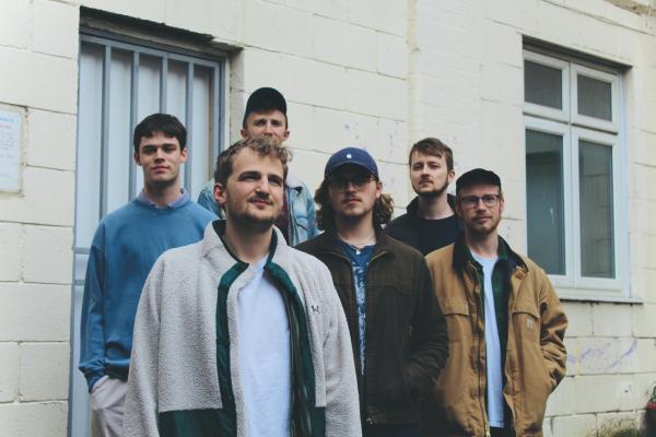 Kasper Rietkerk, Max McLeish, Toby Yapp, Jonah Evans, Benji Bown, and Alex Lockheart, guitar standing next to a wall 