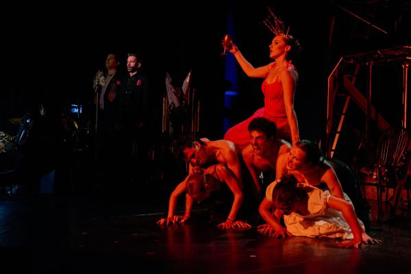 A woman sits seductively on a pile of male bodies