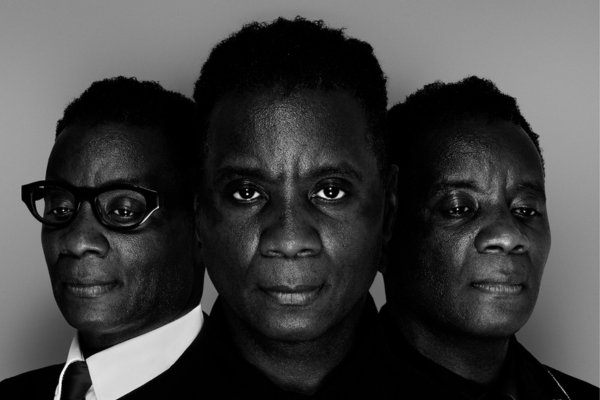 Three men are pictured, the then in the middle looks directly into the camera, and the other two look outwards on slight diagonals.