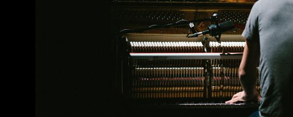 Renowned pianist & composer Nils Frahm is outlined from the back, sat at and playing an upright piano