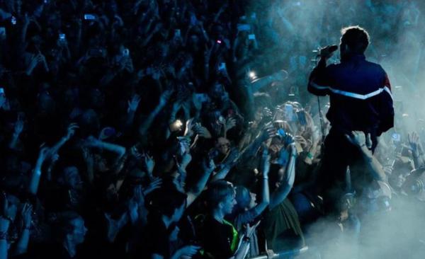 Man on stage in front of large crowd of people holding mic with smoke around him.