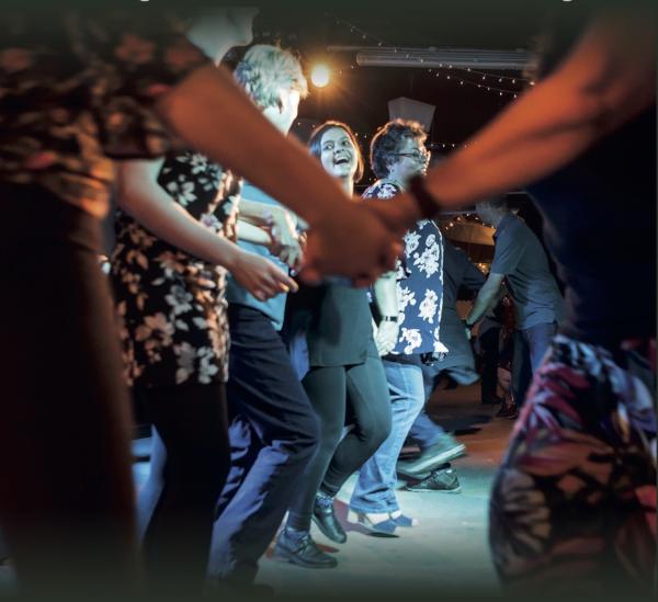 A group of people holding hands, dancing and laughing.