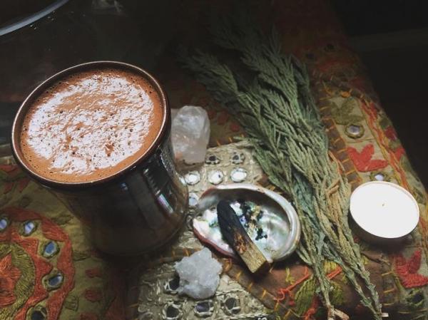 Nice warm cup of froathy cacao, healing crystals and sage, served on a dark wooden table