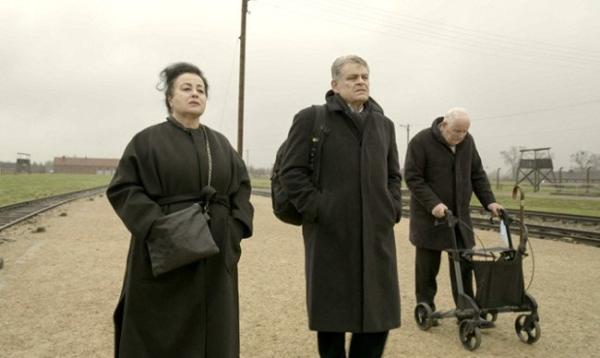 An older woman stands on the left on a gravel road with an older man in the centre and an older man on the right with a mobility aid