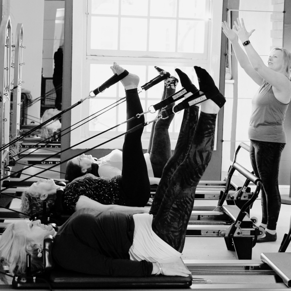 PIlates studio in black and white, the image shows a teacher teaching some women on a Pilates reformer