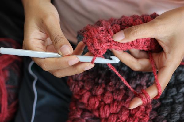 Hands holding chunky red wool and crochet hook