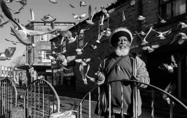 A man in a street with birds flying all around him.