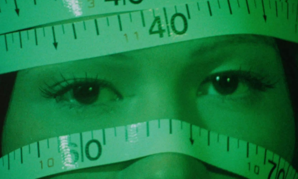 A close-up of a womans eyes with the rest of her face wrapped in measuring tape