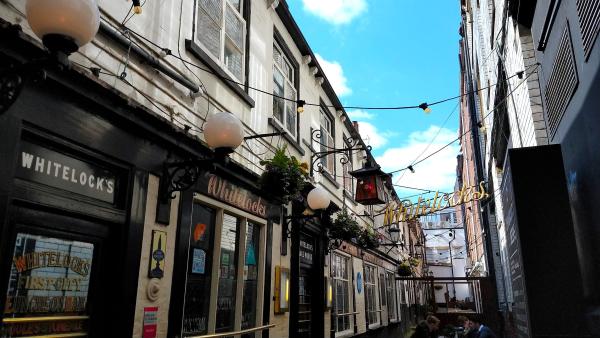 The exterior of Whitelock's Ale House, 17th century tenement cottages converted into a pub in the 18th century, white exterior walls, black door and window frames, with stained glass and painted mirror panels on the doors. The pub is Victorian-era decorated.