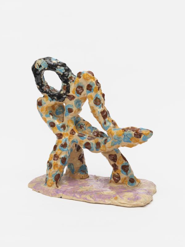 A brightly coloured abstract ceramic sculpture. Almost figure-like - a series of thin, round elements with yellow background and brown and blue spots, sit on a pink base, with a dark brown head-shaped piece on top.